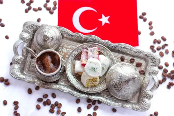 A Turkish coffee service set against the background of the Turkish flag, with a metal cup of coffee, a matching saucer and sugar bowl with intricate designs, and a variety of Turkish delights, symbolizing the patriotic pride and cultural importance of coffee in Turkey.