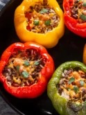 Four bell peppers, vibrant red and yellow, are stuffed with a savory mixture of cooked rice and herbs, all lovingly prepared with olive oil. They're beautifully presented in a black cast iron skillet, as the epitome of the dish known as stuffed peppers with olive oil, ready to be served.